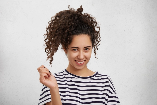 pretty adorable young female with curly pony tail has shy expression